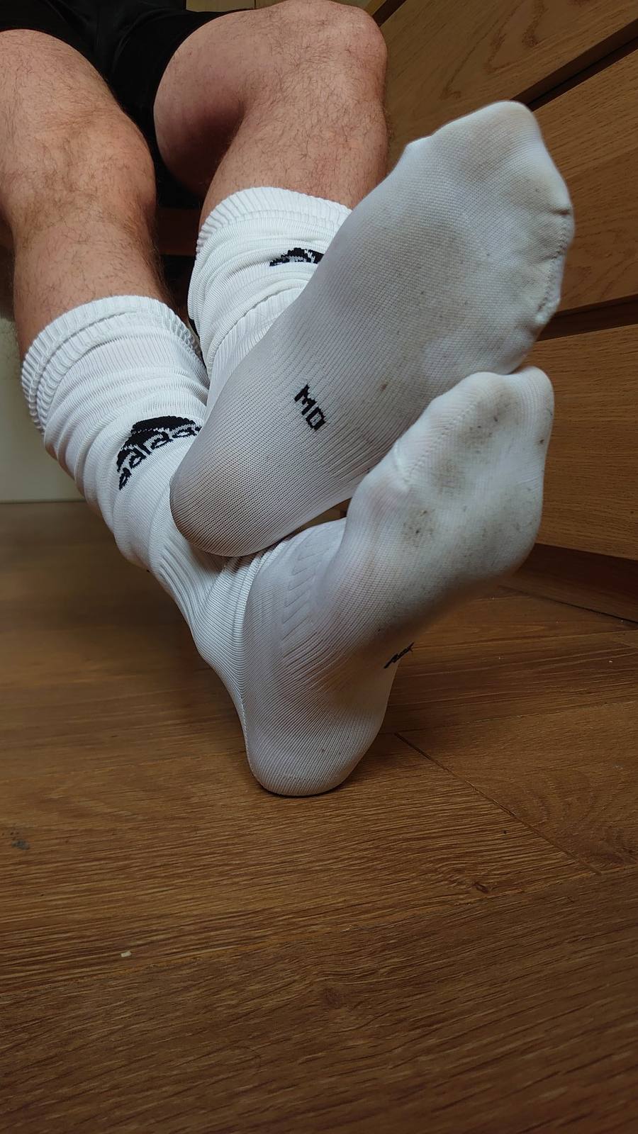 A person's legs and feet are shown wearing white athletic socks indoors.