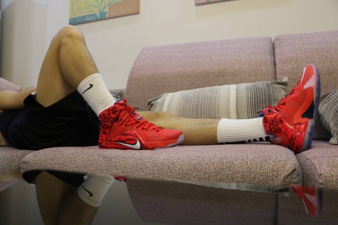 A person reclines on a sofa wearing bright red high-top sneakers and white tube socks.
