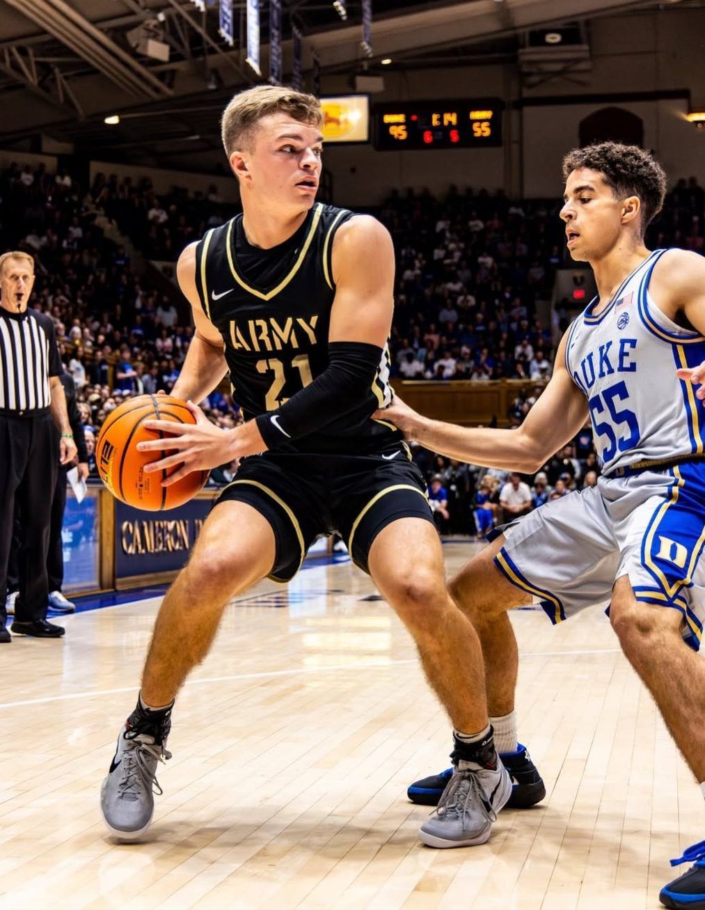 Two young, athletic basketball players in team uniforms compete on the court during a public game.