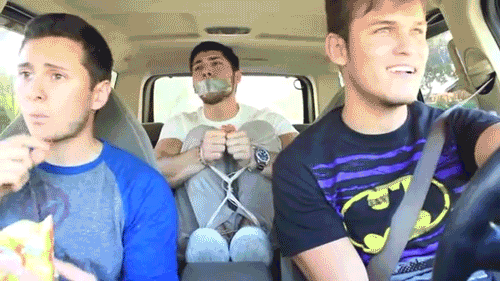 A young man is bound with rope and gagged with duct tape in the back seat of a car while two men sit in the front.