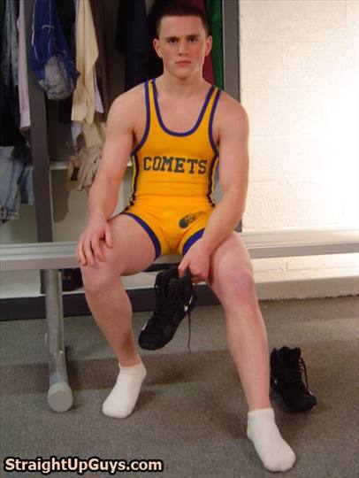 A young athletic man in a yellow and blue wrestling singlet sits on a locker room bench holding one of his black wrestling boots.