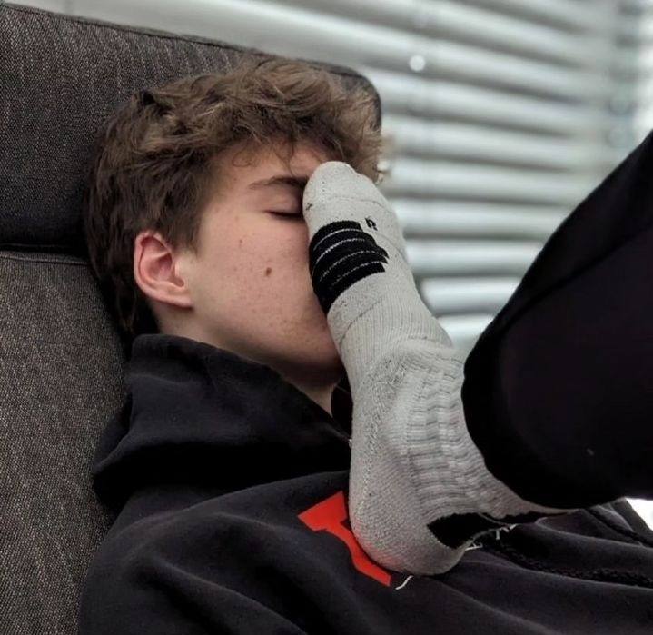 A young man lies on a chair with a gray socked foot pressed against his face.