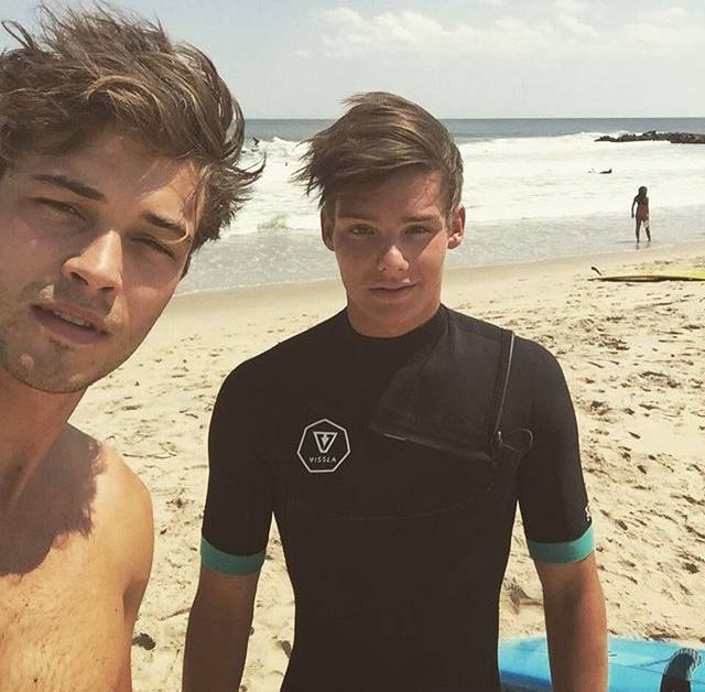 Two young men pose for a selfie on a sunny beach.