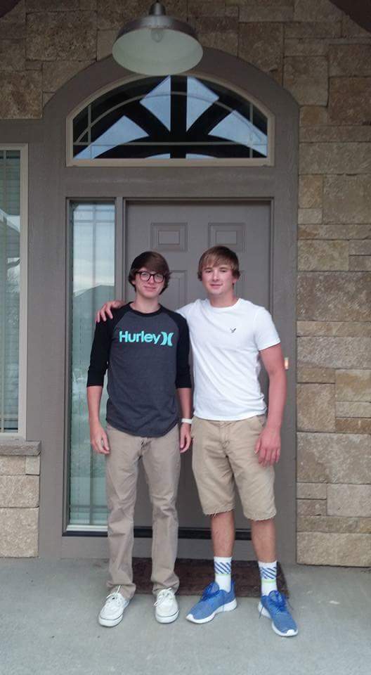 Two young men stand together in front of a house.