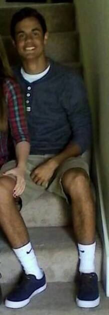 A young man in a blue henley and khaki shorts sits on carpeted stairs wearing white crew socks and blue sneakers.