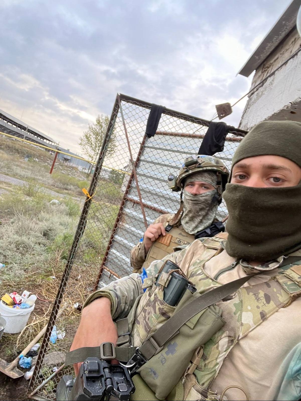 Two men in full military camouflage gear and tactical vests pose outdoors with balaclavas covering their faces.