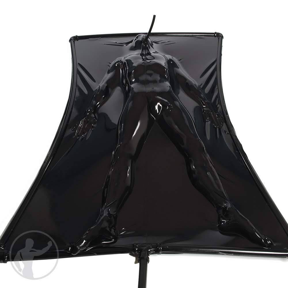 A muscular man is fully encased in a shiny black latex vacuum bed with a single breathing tube for air.