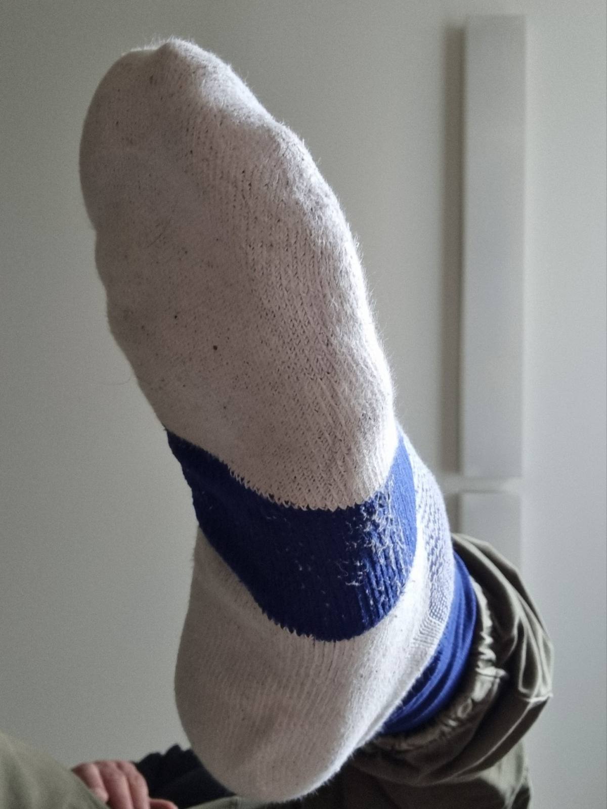 A close-up view of a man's foot wearing a white cotton sport sock with a blue stripe.