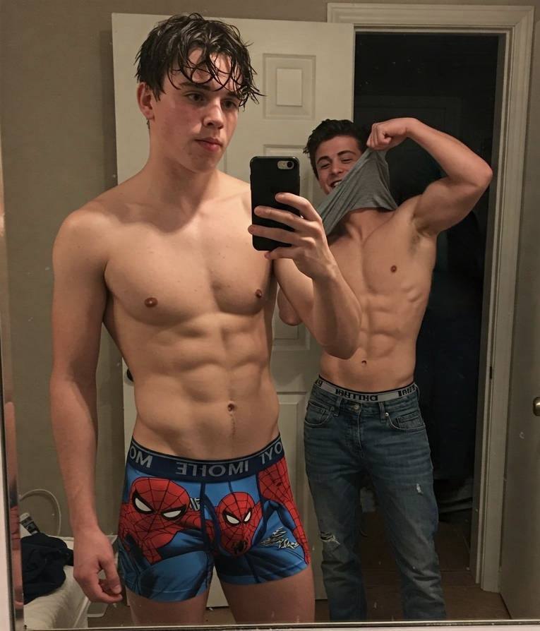 Two athletic young men pose for a mirror selfie wearing underwear and jeans while showing off their abs.