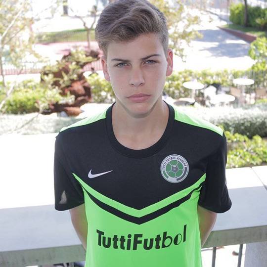 A smooth-faced young man wears a neon green and black football jersey while posing outdoors.