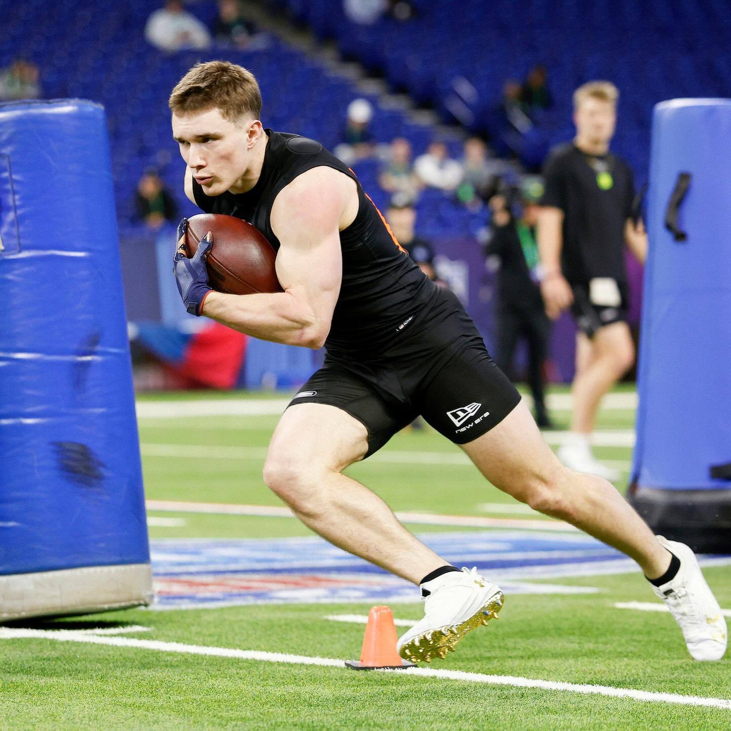A muscular jock in black compression gear runs a football drill on an athletic field.