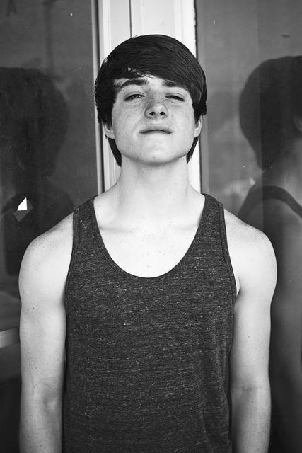 A young man with freckles poses in a tank top.