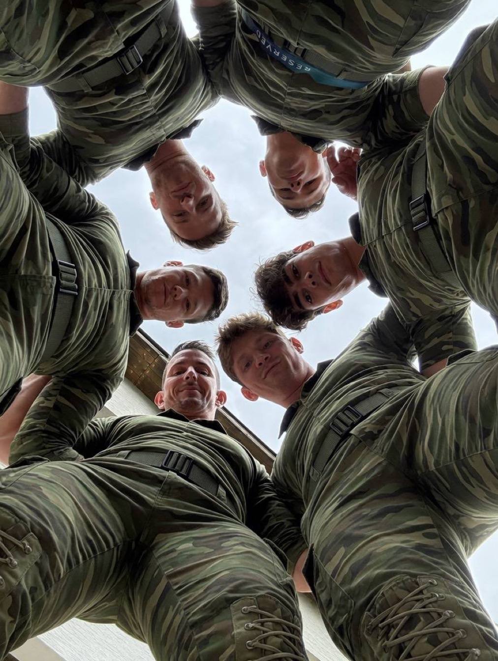 A group of men in camouflage military uniforms look down at the camera.
