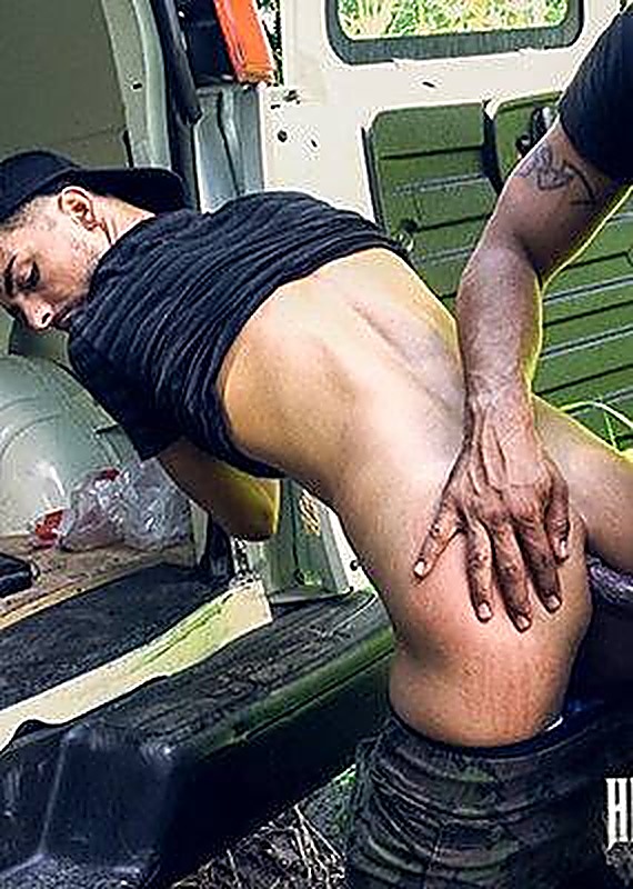 A man in camo pants bends over the open back of a van during an outdoor sexual encounter.