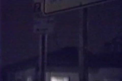 A grainy nighttime shot depicting street signage outdoors in a dark public setting.