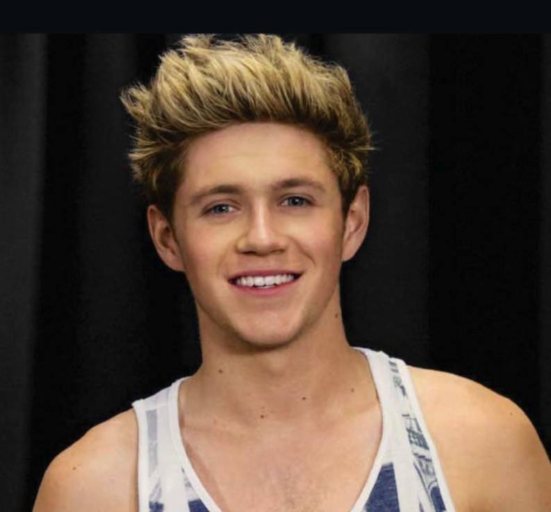 A young man with blond hair smiles while wearing a tank top.