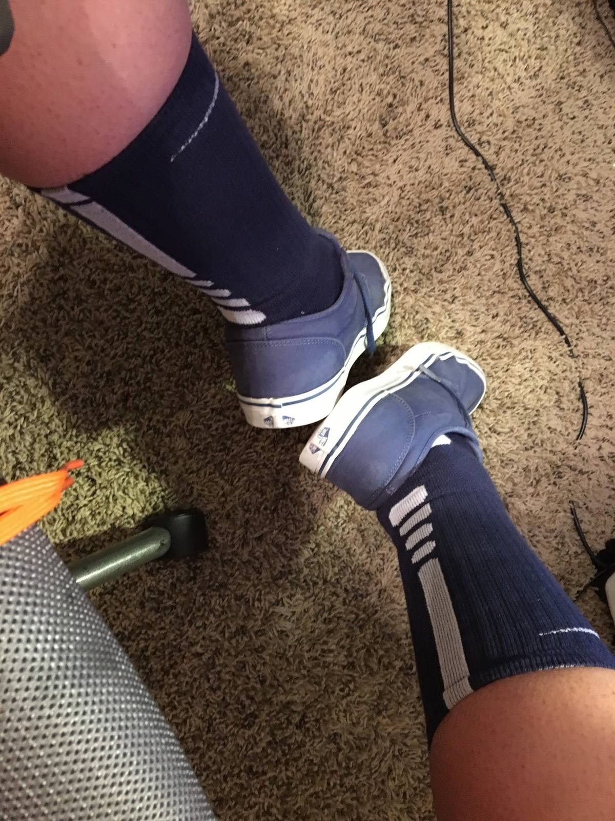 Top-down view of a person wearing blue athletic crew socks and blue canvas sneakers while sitting indoors.