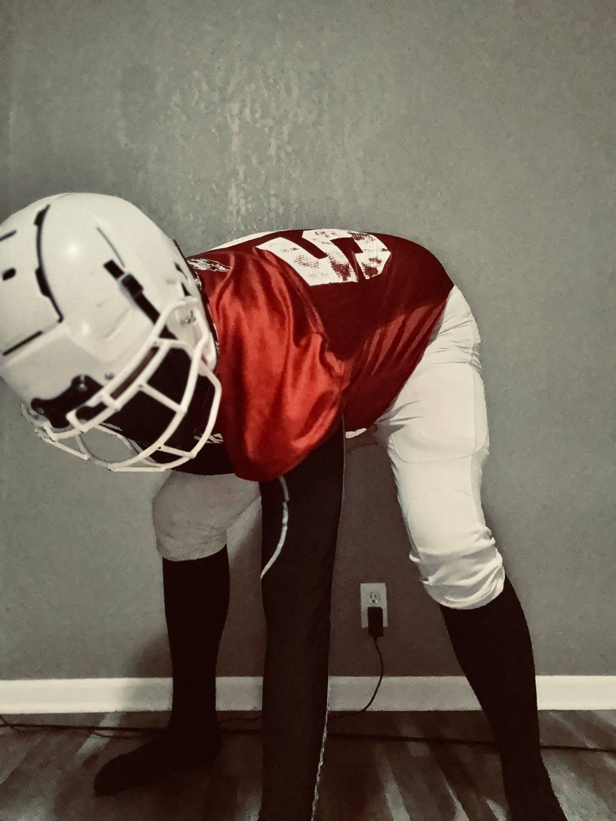 A person in a full American football kit, including a helmet, jersey, and padded pants over compression tights, leans forward in a presenting stance.