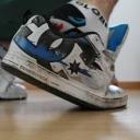 A person wears white and blue sneakers with white patterned socks on a wooden floor.
