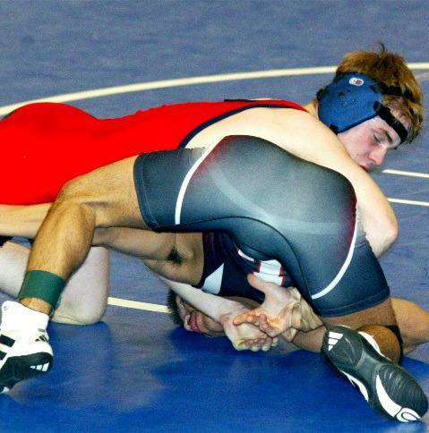 Two young wrestlers in spandex singlets engage in a grappling match on a blue mat.