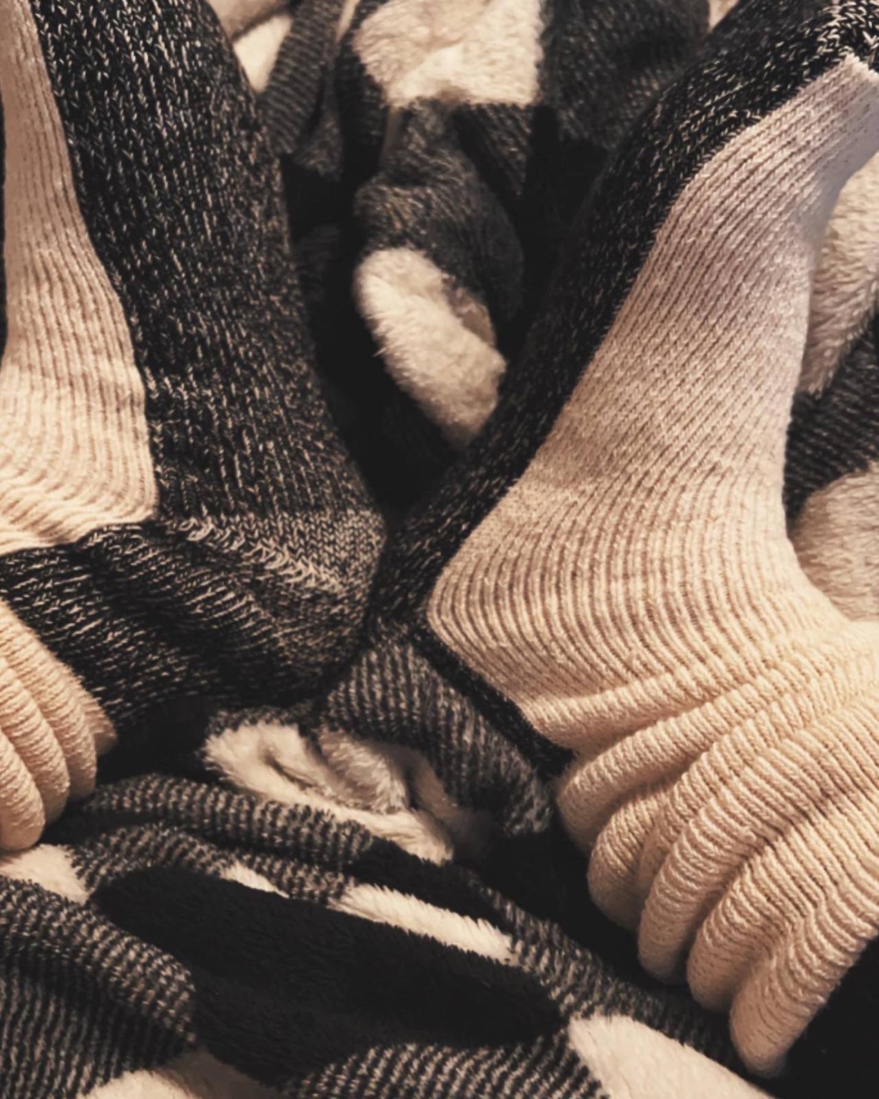 A close-up view of a pair of feet wearing thick, ribbed grey and white wool socks resting on a plush blanket.
