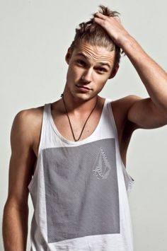 A young man with a man bun poses in a white tank top.