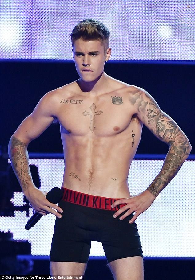 A shirtless man with tattoos performs on stage in black boxer briefs.