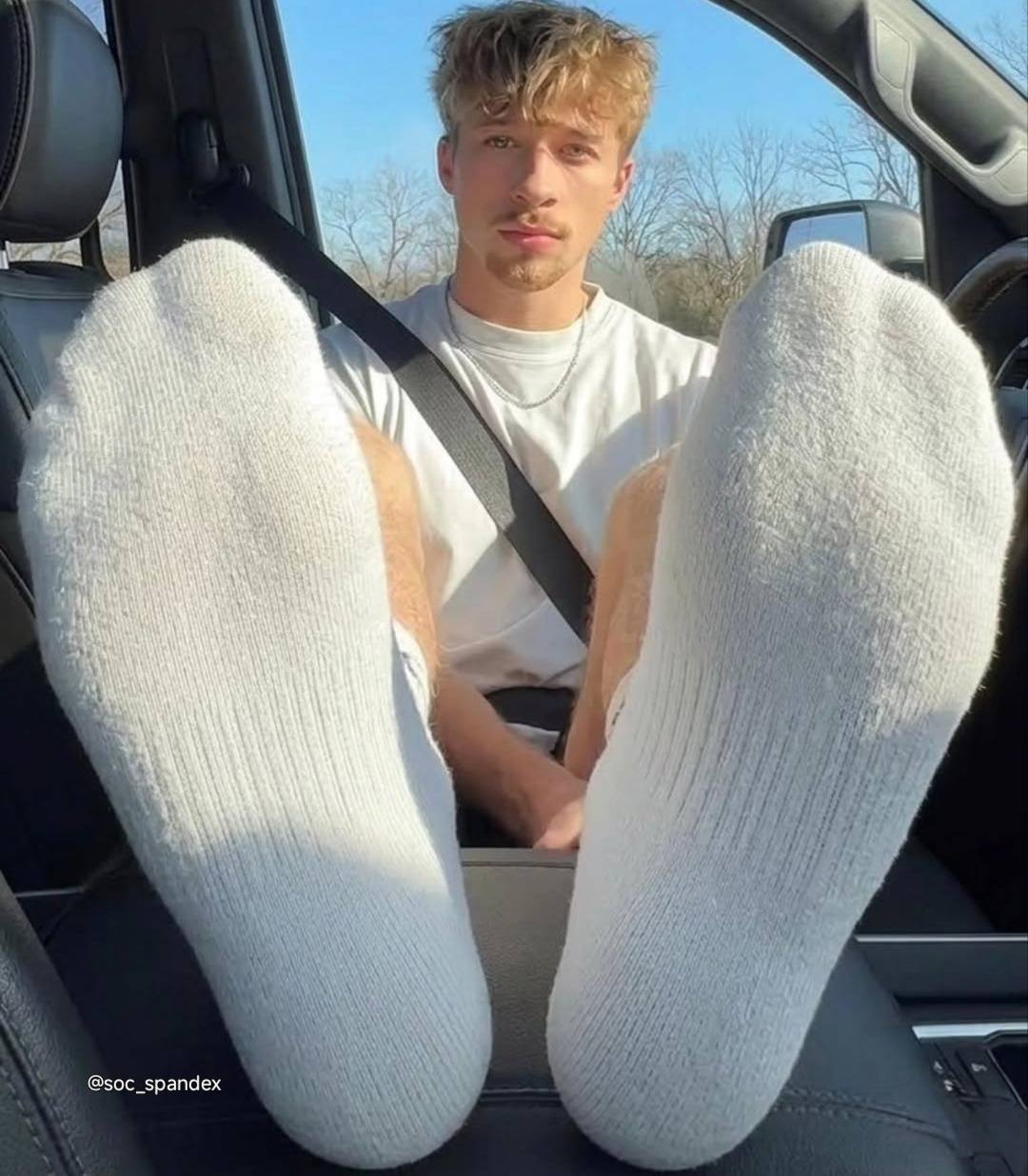 A young man with white socks on his feet is sitting in a car.