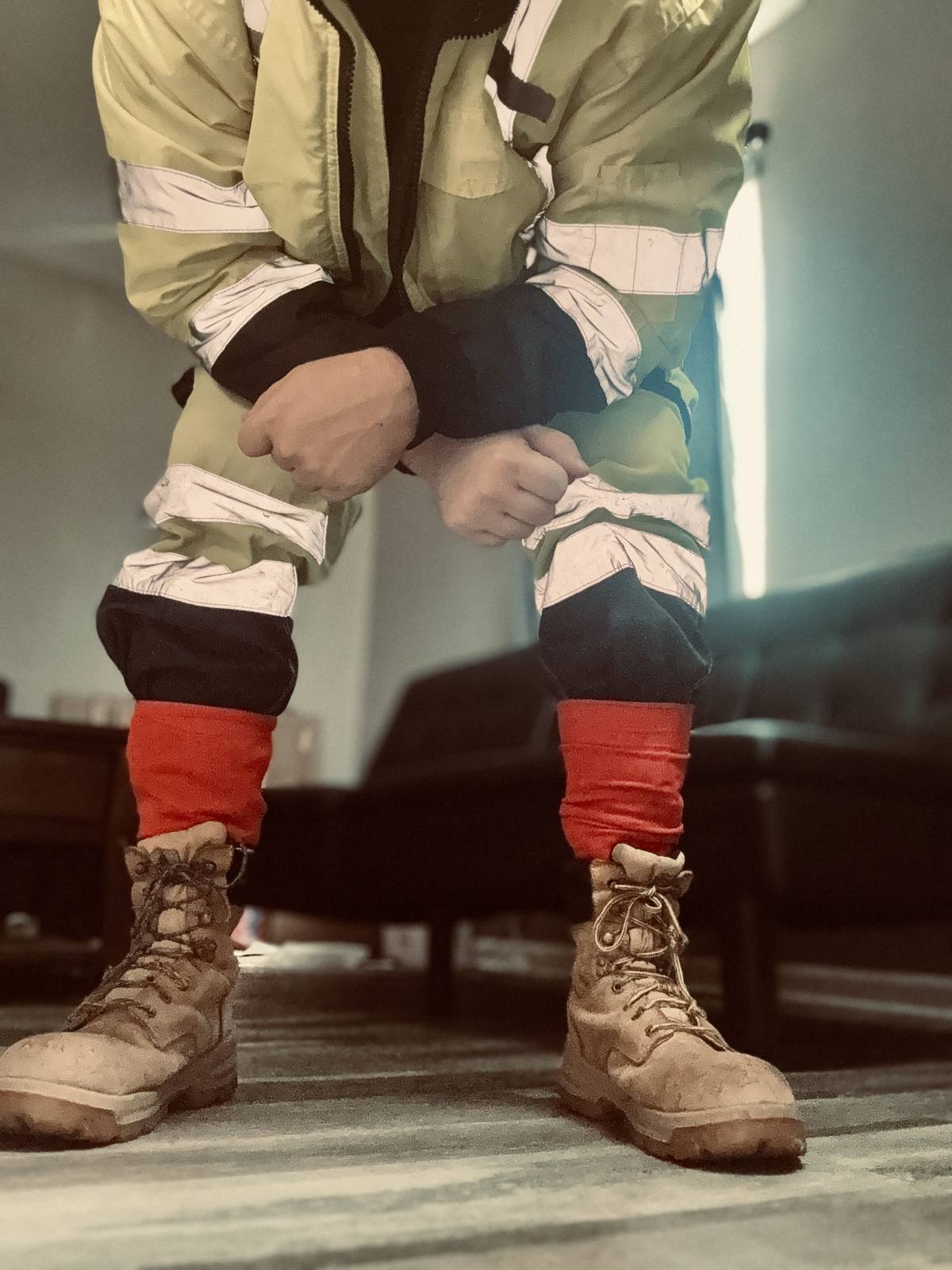 A man in a full hi-vis construction uniform and tan work boots leans forward in an indoor setting.