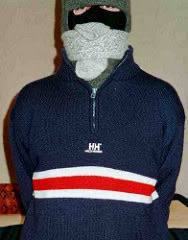 A person wearing a navy knit sweater has their face obscured by a balaclava, a knit cap, and thick wool socks wrapped tightly around their head.