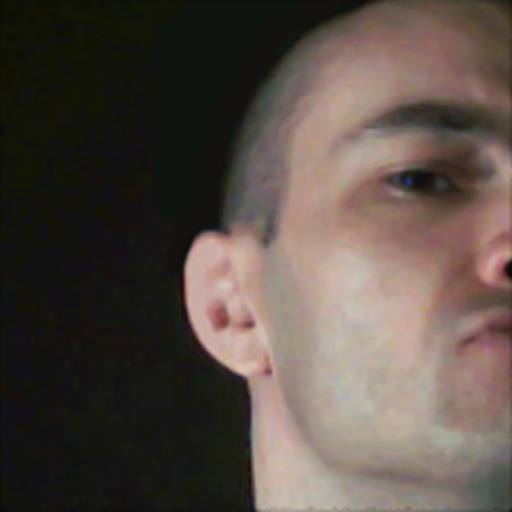 A close-up portrait of a man with a buzzcut looking into the camera against a dark background.