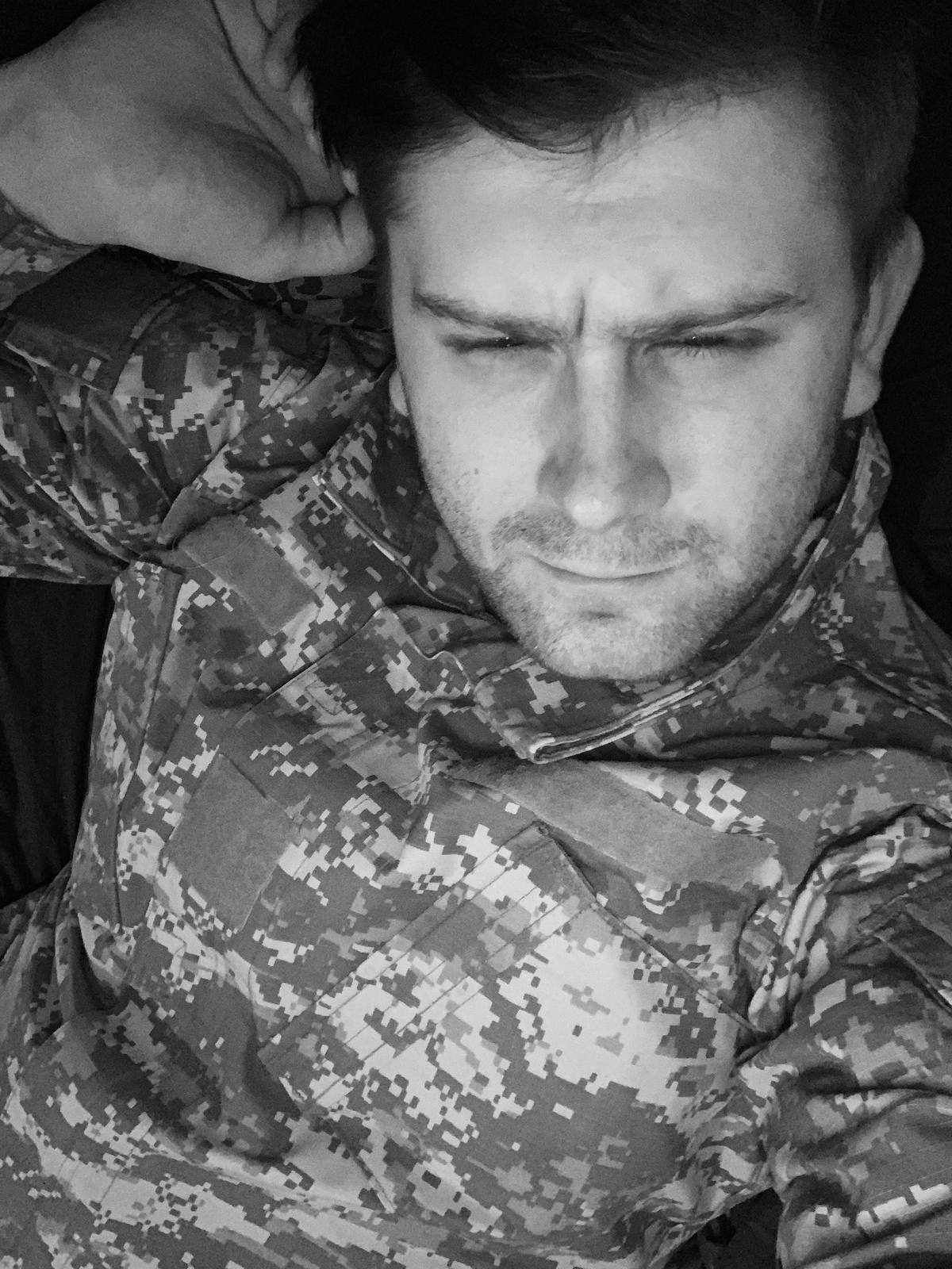 A black and white selfie of a scruffy man wearing a digital camouflage military uniform.