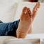 A person's bare feet rest on a white sofa.