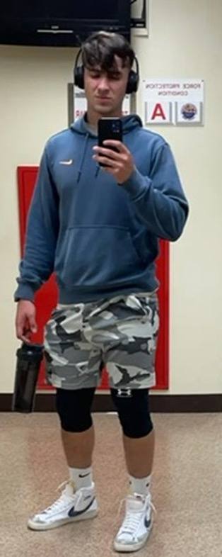 A young jock in a blue hoodie and camo shorts takes a mirror selfie in a gym setting.