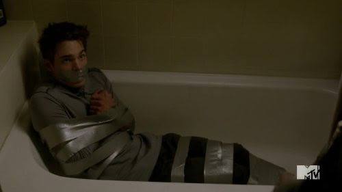 A young man lies bound with heavy silver duct tape around his arms and legs while gagged inside a bathtub.