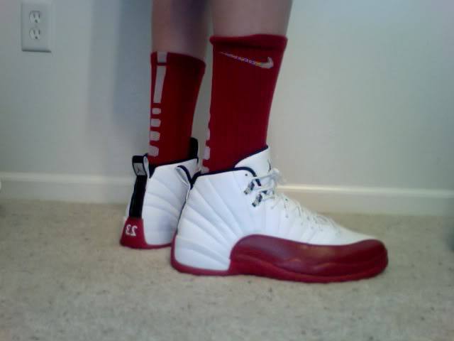 A person stands on a carpeted floor wearing red socks and white and red sneakers.