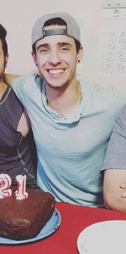 A young man with a backwards baseball cap smiles behind a 21st birthday cake.