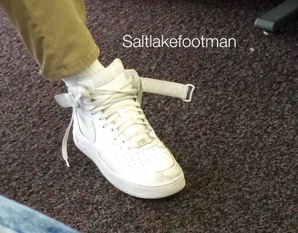 A close-up view of a foot wearing a white Nike Air Force 1 high-top sneaker with an undone ankle strap and white tube socks.