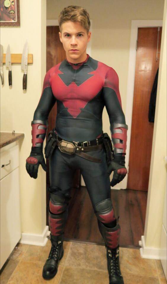 A young man in a red and black full body uniform suit poses indoors.