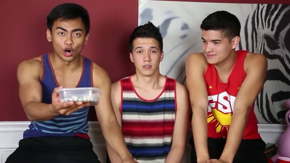 Three young men in tank tops are engaged in a casual indoor activity.