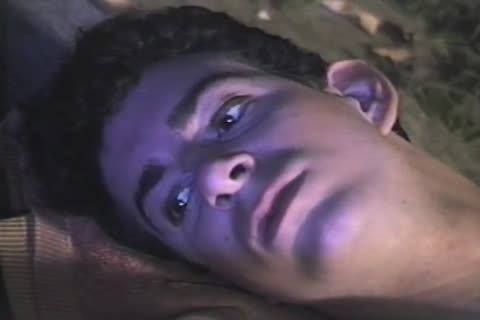 A close-up view of a young man with dark curly hair lying down under dramatic purple lighting.