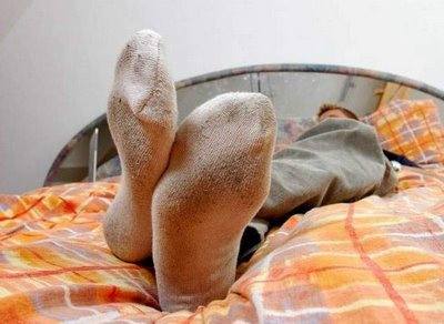 A person is relaxing on a bed with their dirty socks visible.