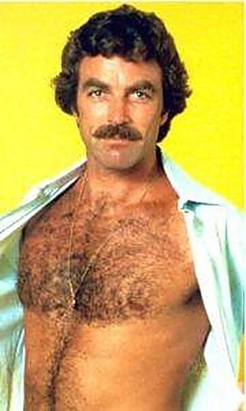 A mature man with a thick mustache displays his hairy chest through an open light blue shirt in front of a yellow backdrop.