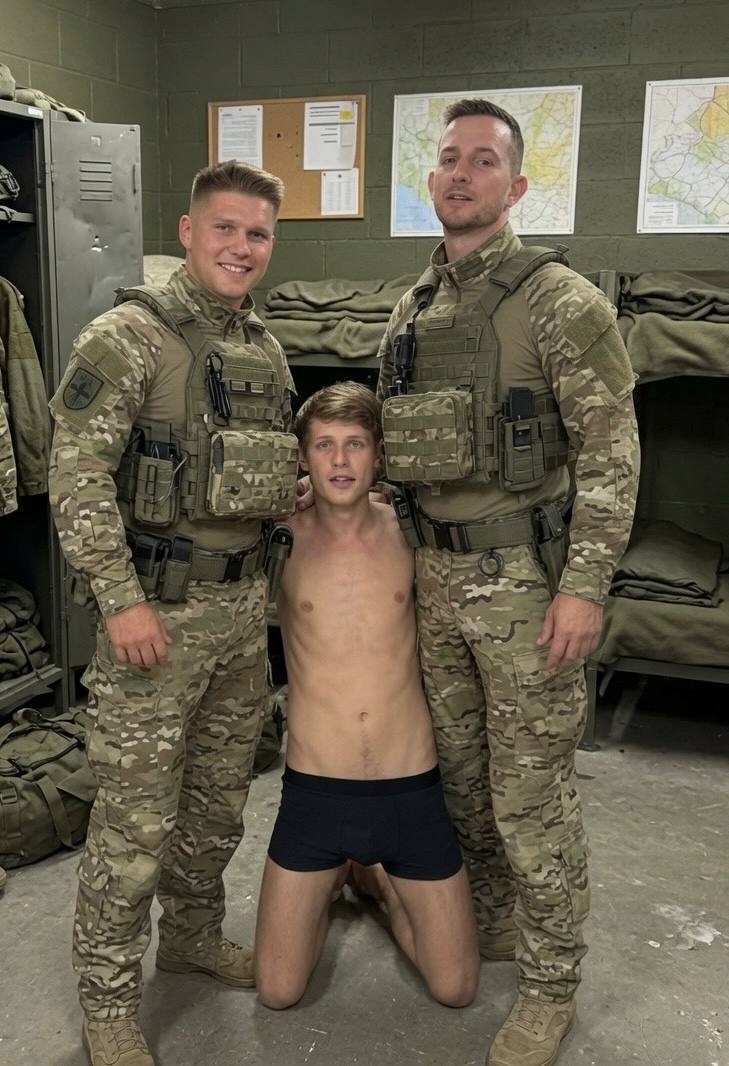 A shirtless man in boxer briefs kneels on the floor between two men dressed in full military camouflage uniforms and tactical gear inside a barracks.