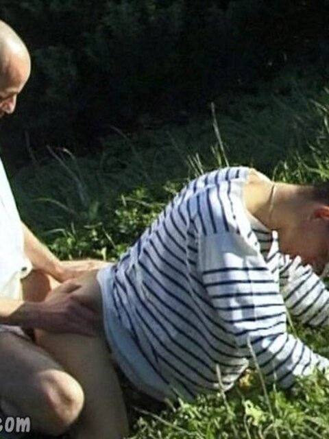 Two men engage in an intimate outdoor encounter while surrounded by grass and foliage.