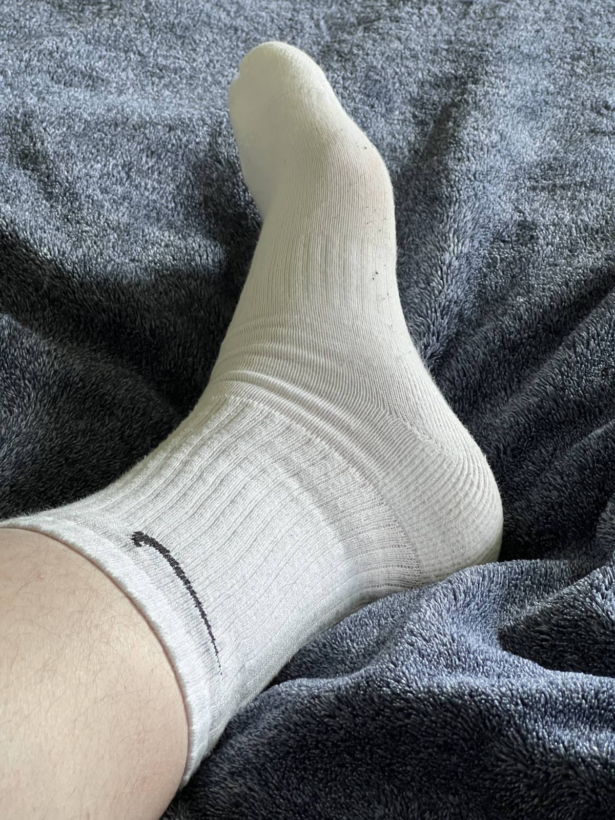 A close-up view of a foot wearing a white athletic sock resting on a plush gray blanket.